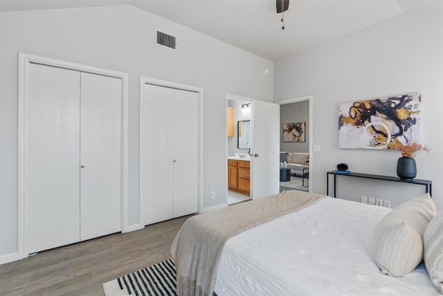 bedroom with multiple closets, ensuite bathroom, lofted ceiling, and light wood-type flooring