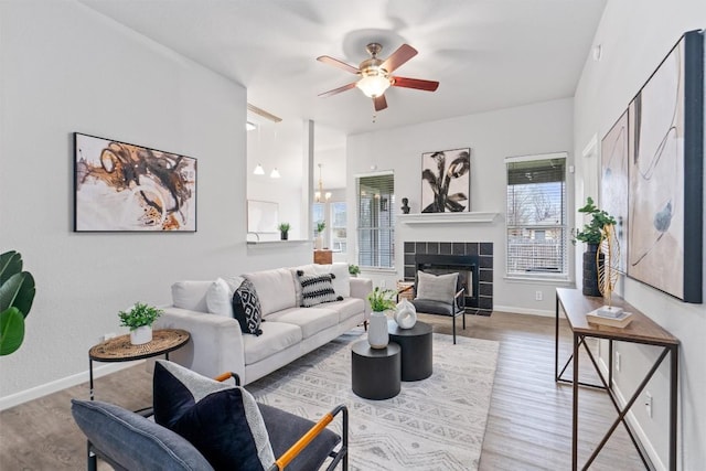 living room with ceiling fan with notable chandelier, a fireplace, and light hardwood / wood-style floors