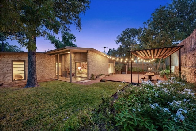 back house at dusk with a patio and a yard