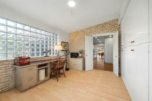 home office with brick wall, lofted ceiling, built in desk, and light wood-type flooring