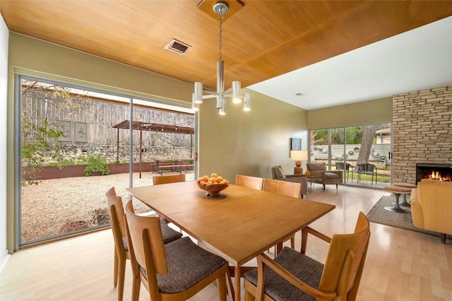 dining room featuring a large fireplace, light hardwood / wood-style flooring, and wooden ceiling