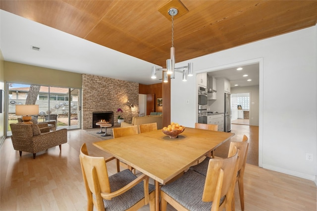 dining area featuring wooden ceiling, a brick fireplace, and light wood-type flooring