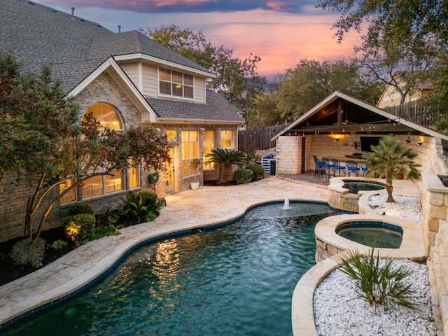 pool at dusk featuring an in ground hot tub and a patio