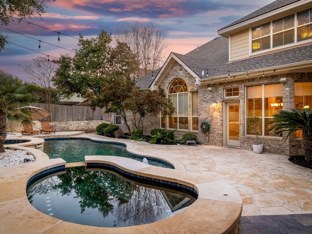 pool at dusk with an in ground hot tub and a patio area