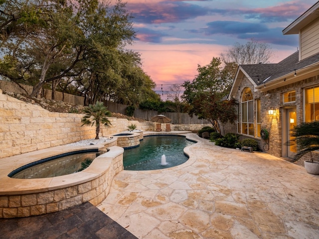 pool at dusk featuring a patio, pool water feature, and an in ground hot tub