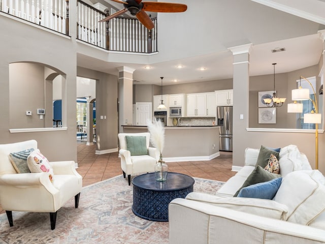 living room featuring decorative columns, ceiling fan with notable chandelier, light tile patterned floors, and high vaulted ceiling