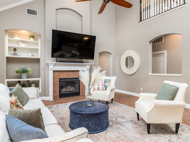 tiled living room featuring built in features, ceiling fan, a high ceiling, a fireplace, and ornamental molding