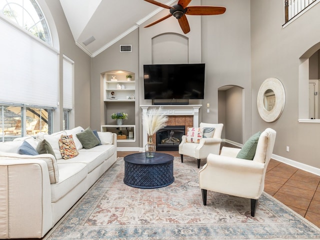 living room with high vaulted ceiling, a tiled fireplace, ceiling fan, tile patterned floors, and built in shelves