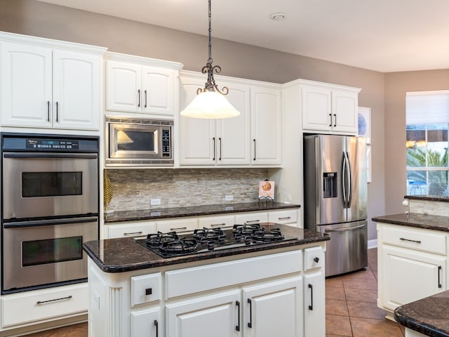 kitchen with tile patterned floors, hanging light fixtures, appliances with stainless steel finishes, white cabinets, and backsplash