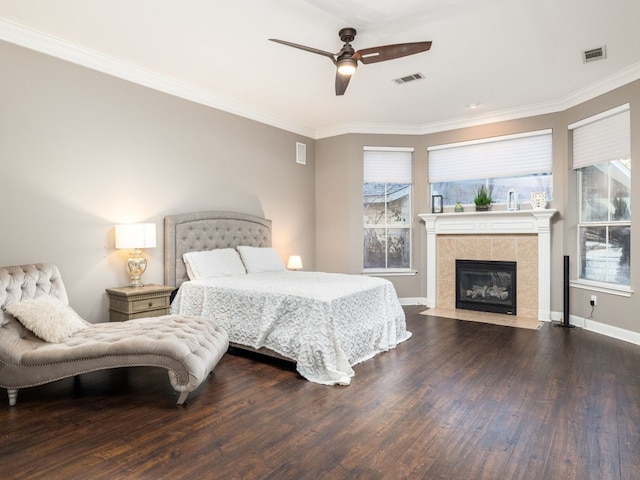 bedroom featuring crown molding, ceiling fan, wood-type flooring, and a tile fireplace