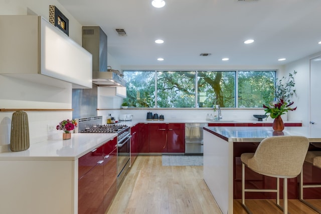 kitchen with light hardwood / wood-style flooring, a breakfast bar, tasteful backsplash, stainless steel range with gas cooktop, and exhaust hood