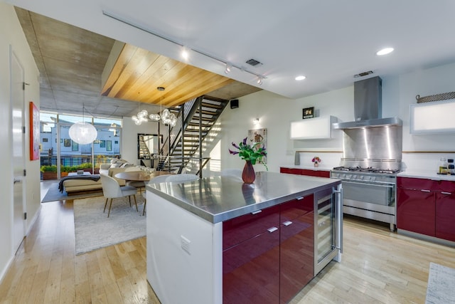 kitchen featuring wine cooler, high end stainless steel range oven, stainless steel counters, light hardwood / wood-style floors, and wall chimney range hood