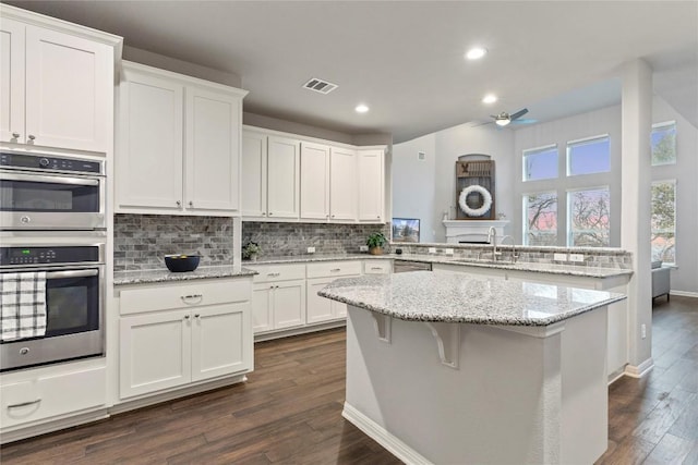 kitchen with light stone countertops, stainless steel double oven, white cabinets, and kitchen peninsula