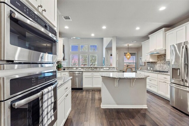 kitchen featuring pendant lighting, dark wood-type flooring, appliances with stainless steel finishes, white cabinetry, and light stone countertops