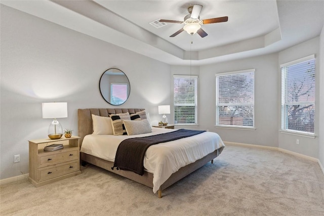 bedroom featuring light carpet, ceiling fan, and a tray ceiling