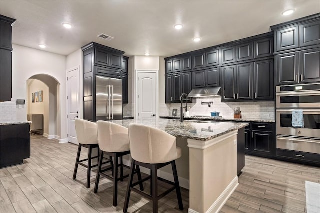 kitchen with a breakfast bar, appliances with stainless steel finishes, backsplash, light stone counters, and light wood-type flooring