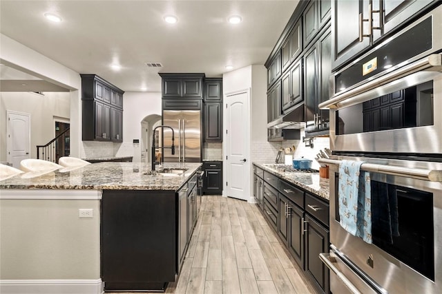 2513 Long Lasso Pass, Leander, TX 78641 - kitchen with appliances with stainless steel finishes, light wood finished floors, decorative backsplash, light stone counters, and a kitchen island with sink