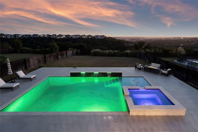 pool at dusk featuring an in ground hot tub and a patio