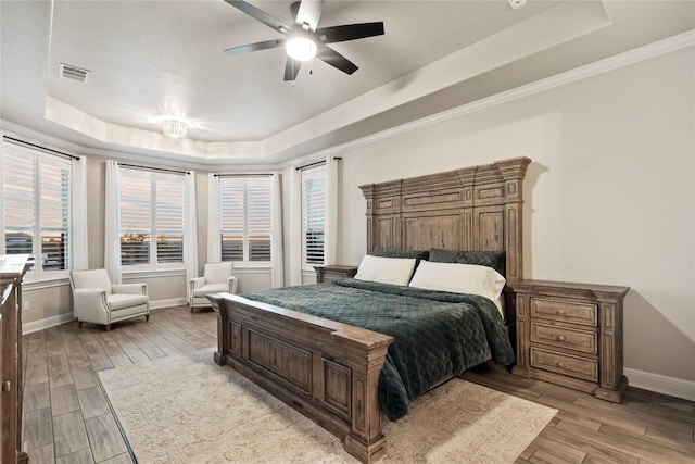 bedroom with crown molding, a tray ceiling, light hardwood / wood-style floors, and ceiling fan