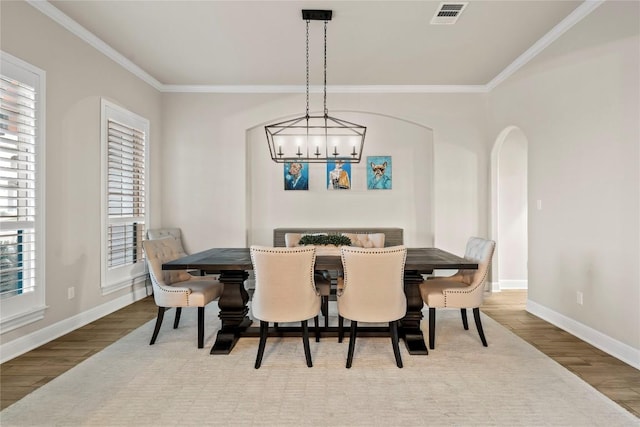 dining space with wood-type flooring, ornamental molding, and an inviting chandelier