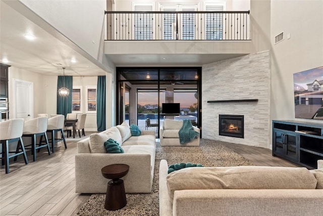 living room featuring wood-type flooring, a stone fireplace, and a towering ceiling