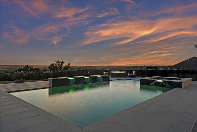 pool at dusk featuring pool water feature and an in ground hot tub