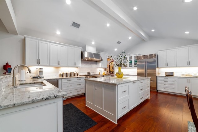 kitchen featuring wall chimney range hood, a kitchen island, light stone countertops, and appliances with stainless steel finishes