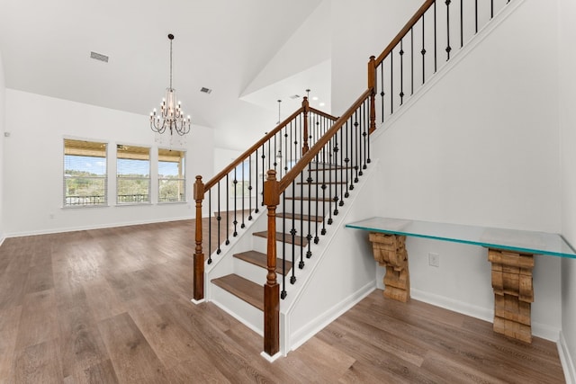 staircase with hardwood / wood-style flooring, a chandelier, and high vaulted ceiling