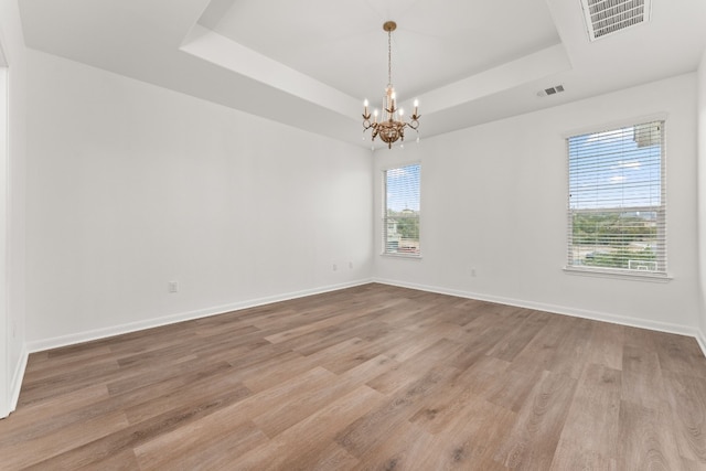 spare room with a chandelier, light wood-type flooring, and a tray ceiling