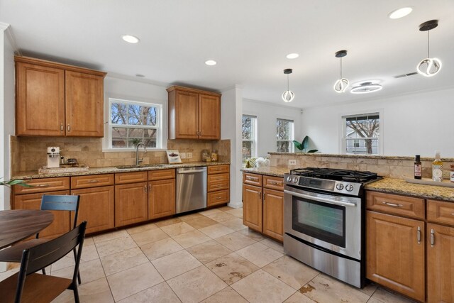 kitchen with light stone counters, appliances with stainless steel finishes, sink, and hanging light fixtures