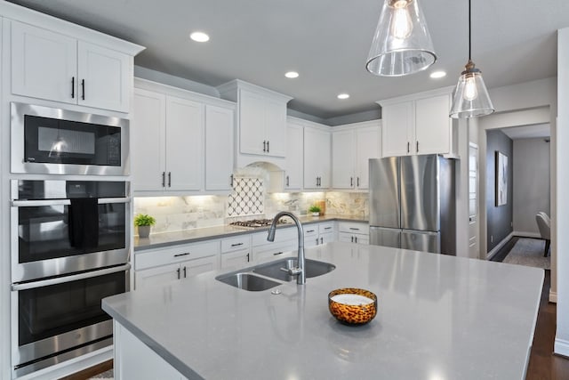 kitchen with sink, appliances with stainless steel finishes, white cabinets, a center island with sink, and decorative light fixtures