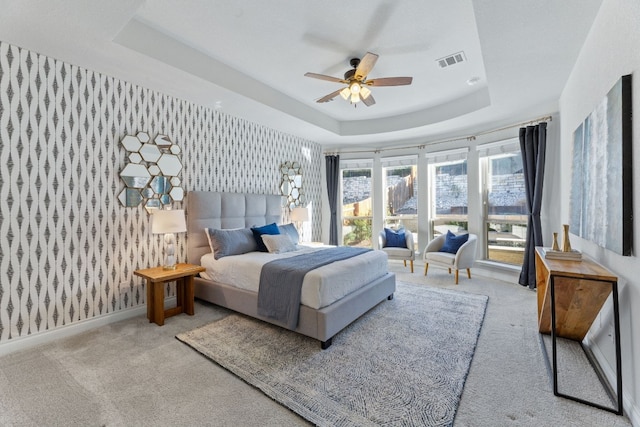 carpeted bedroom with a raised ceiling and ceiling fan