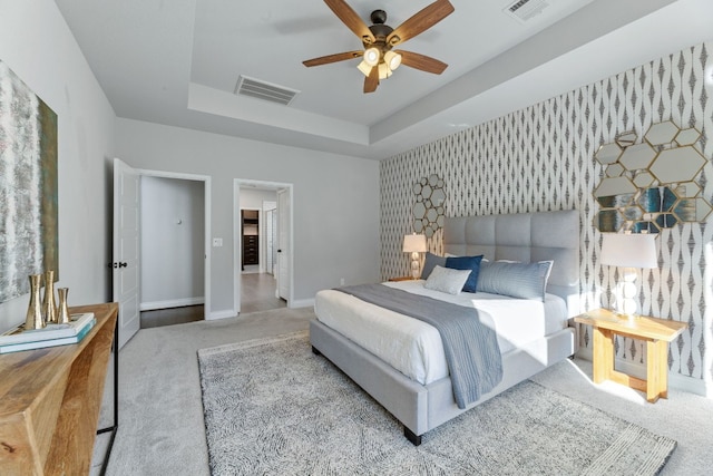 bedroom with light carpet, a raised ceiling, and ceiling fan