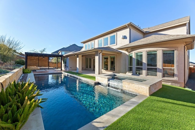 rear view of property featuring a swimming pool with hot tub, a patio area, pool water feature, and a lawn