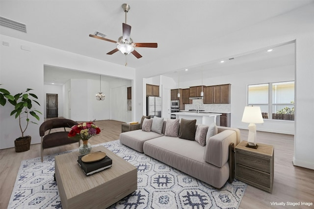 living room with ceiling fan with notable chandelier and light hardwood / wood-style flooring