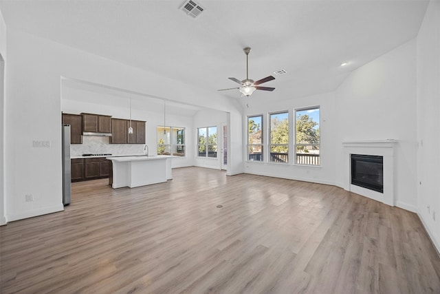 unfurnished living room with ceiling fan, lofted ceiling, sink, and light hardwood / wood-style flooring