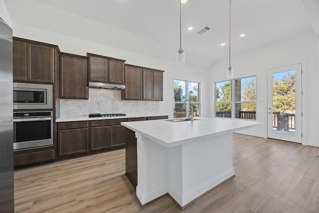 kitchen featuring appliances with stainless steel finishes, decorative light fixtures, an island with sink, sink, and decorative backsplash