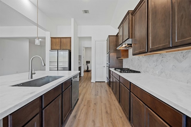 kitchen featuring sink, light hardwood / wood-style flooring, appliances with stainless steel finishes, backsplash, and hanging light fixtures