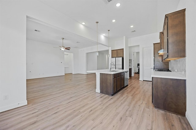 kitchen featuring sink, a kitchen island with sink, hanging light fixtures, and light wood-type flooring