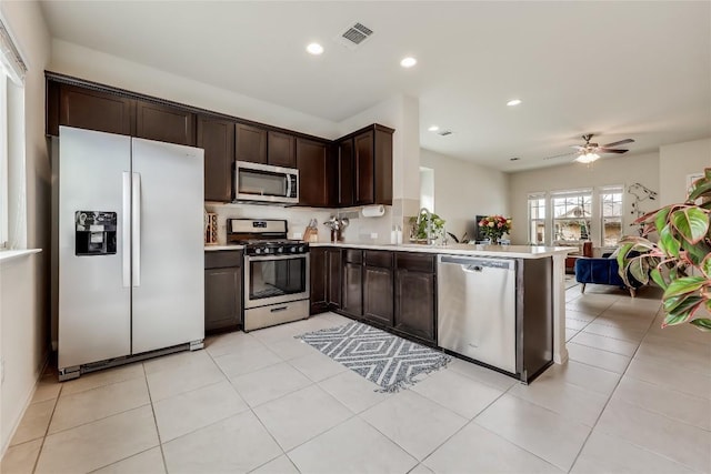 kitchen featuring ceiling fan, appliances with stainless steel finishes, dark brown cabinetry, light tile patterned flooring, and kitchen peninsula