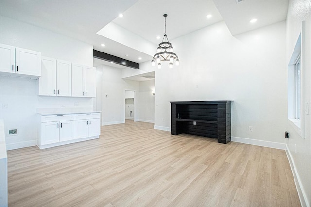 unfurnished living room with a towering ceiling, an inviting chandelier, and light wood-type flooring