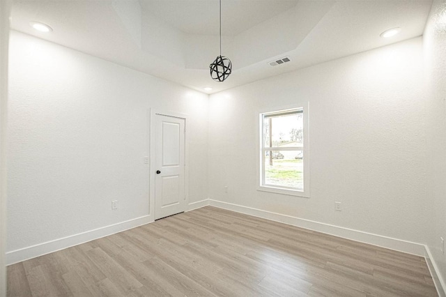 unfurnished room with a raised ceiling and light hardwood / wood-style flooring