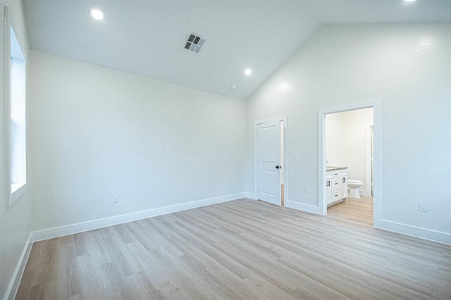 unfurnished bedroom featuring ensuite bath, high vaulted ceiling, and light hardwood / wood-style flooring