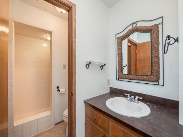 bathroom featuring vanity, a tile shower, tile patterned floors, and toilet