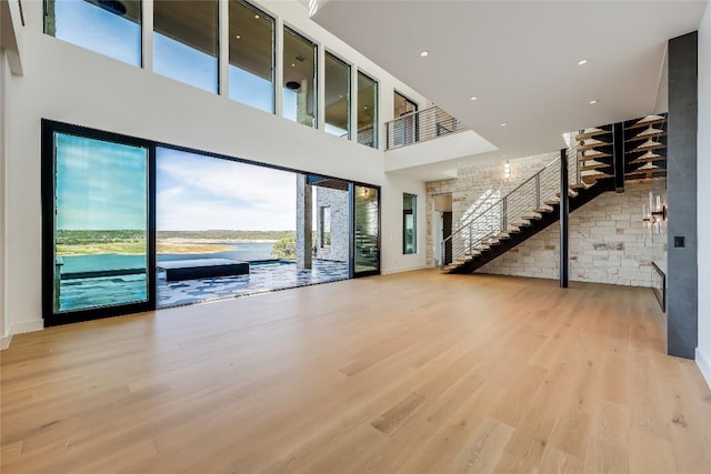 unfurnished living room featuring a high ceiling, a water view, and light hardwood / wood-style floors