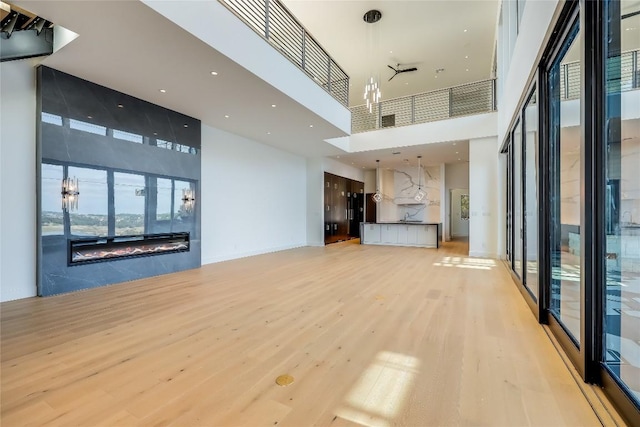 unfurnished living room with light hardwood / wood-style flooring, a premium fireplace, and a high ceiling