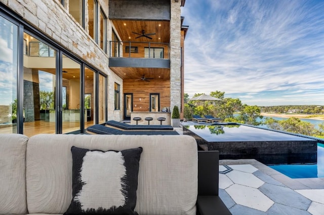 view of patio featuring ceiling fan, a balcony, an outdoor living space, and a water view