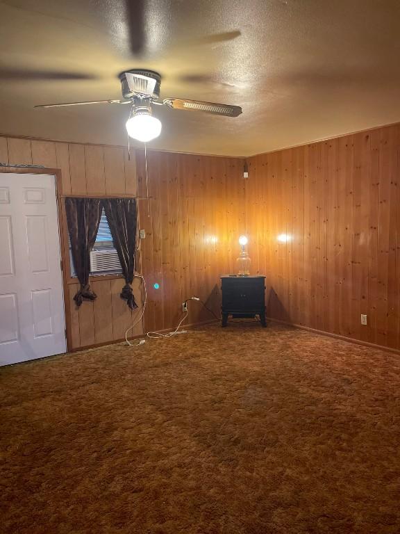 carpeted spare room featuring a textured ceiling, ceiling fan, and wood walls