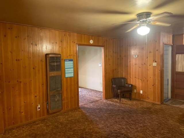 interior space featuring ceiling fan, heating unit, dark carpet, and wood walls