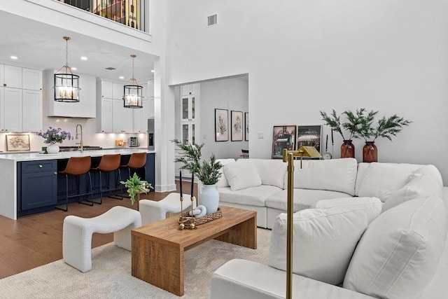 living area with visible vents, wood finished floors, a towering ceiling, and recessed lighting